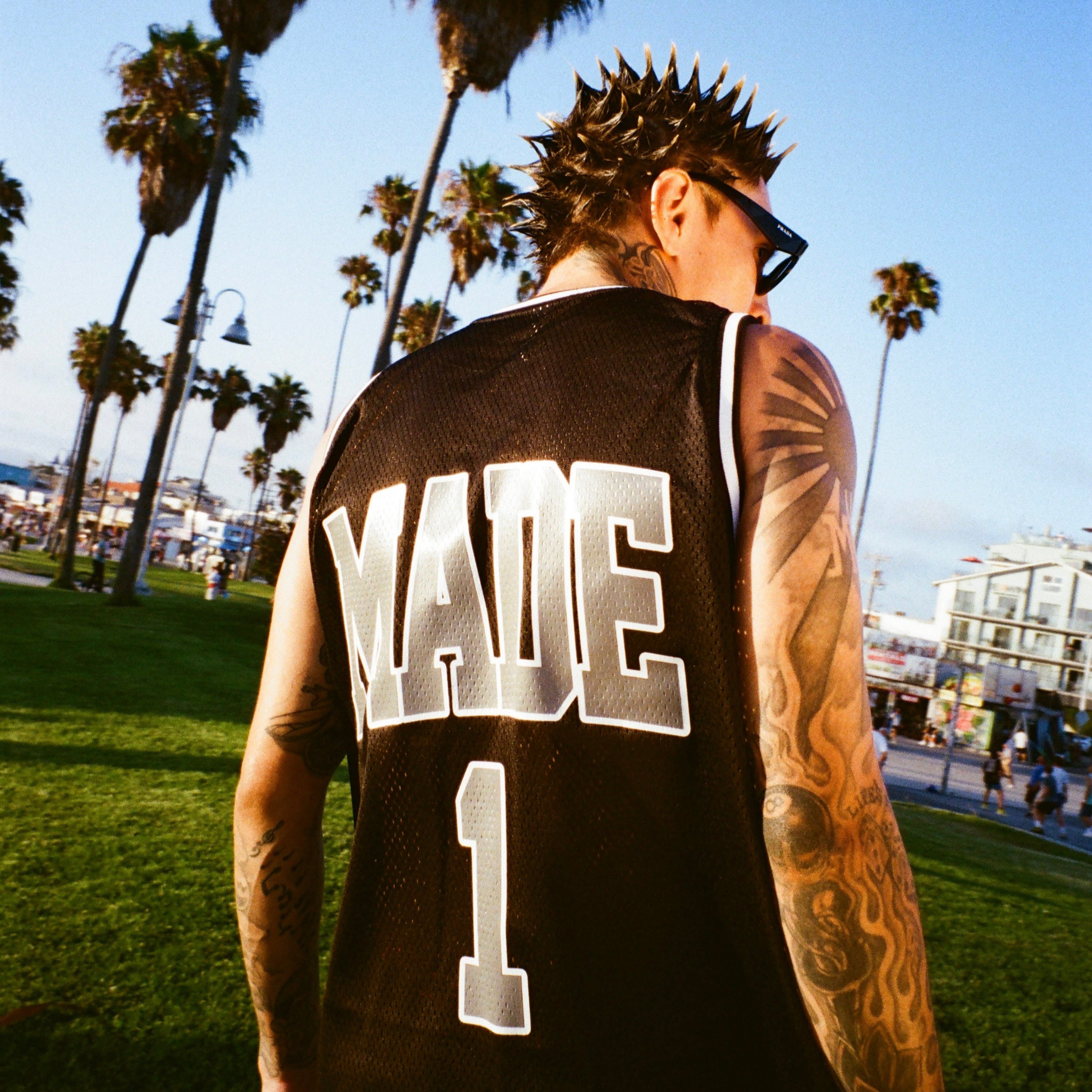 Person wearing a black jersey with MADE 1' on the back, standing in a park with palm trees.