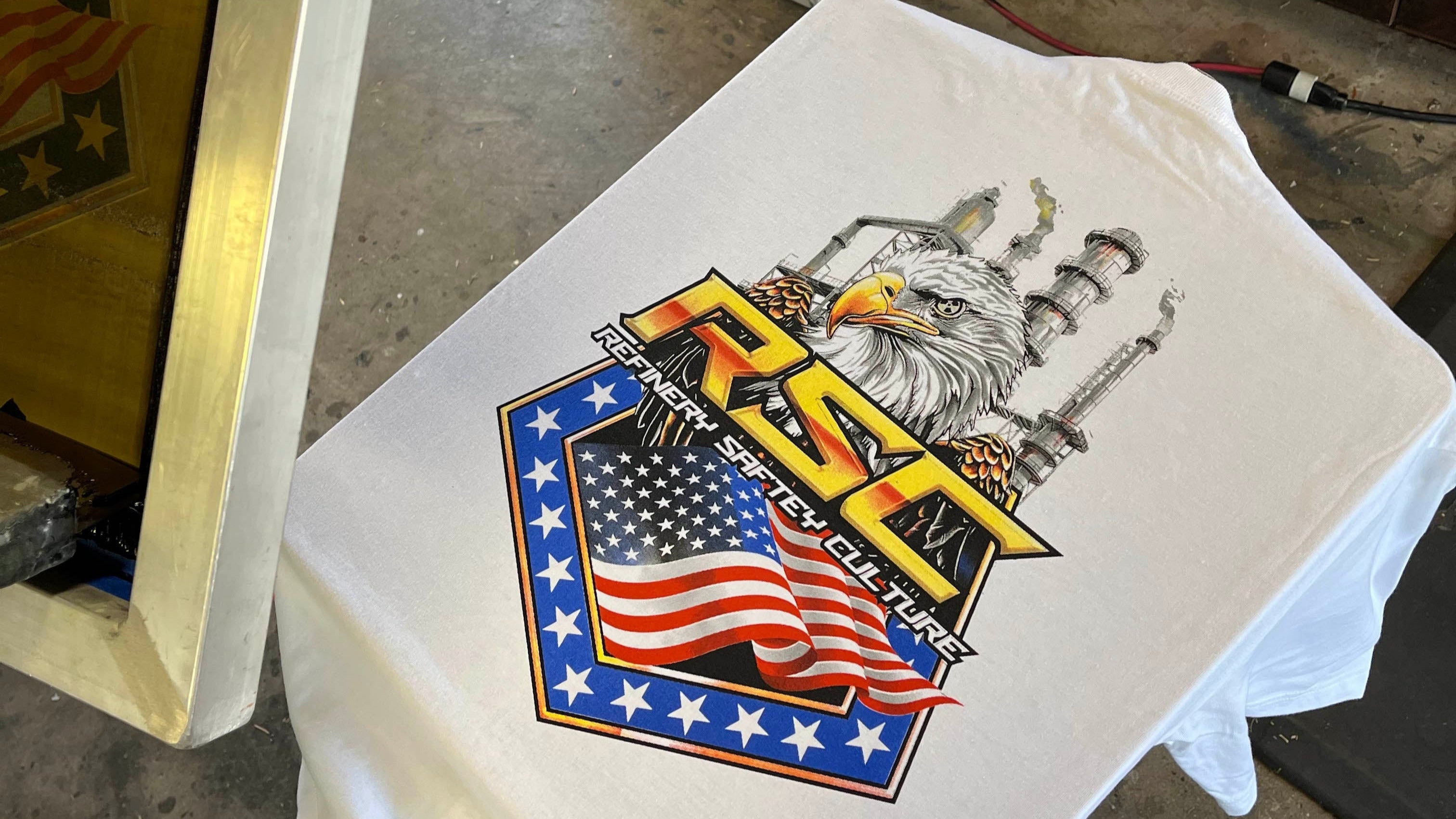 White t-shirt with a graphic design featuring an eagle and American flag on a workbench.