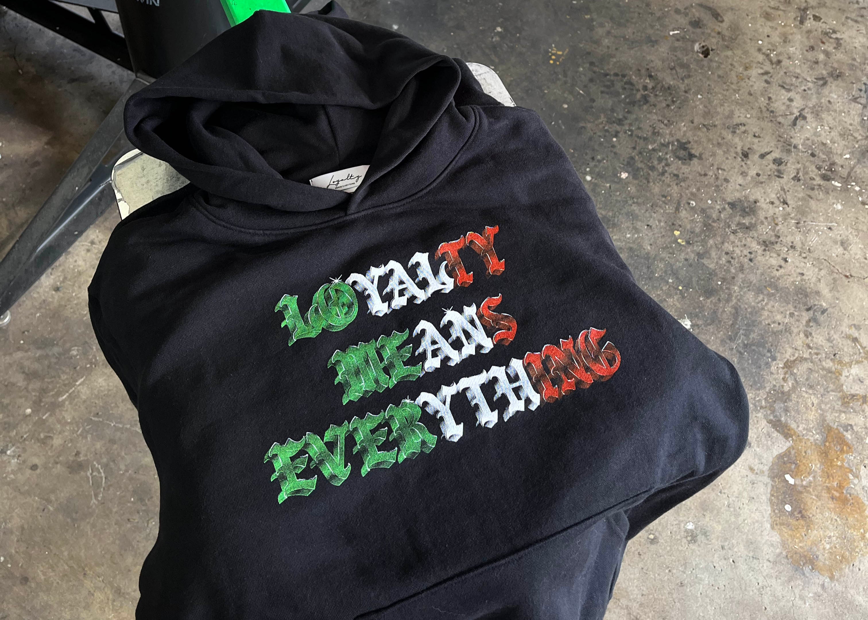 Black hoodie with colorful mexico  text on a concrete floor with screen printing equipment in the background